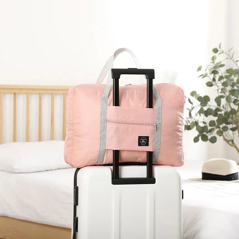 Pink folding travel bag on a white suitcase with a bed and plant in the background