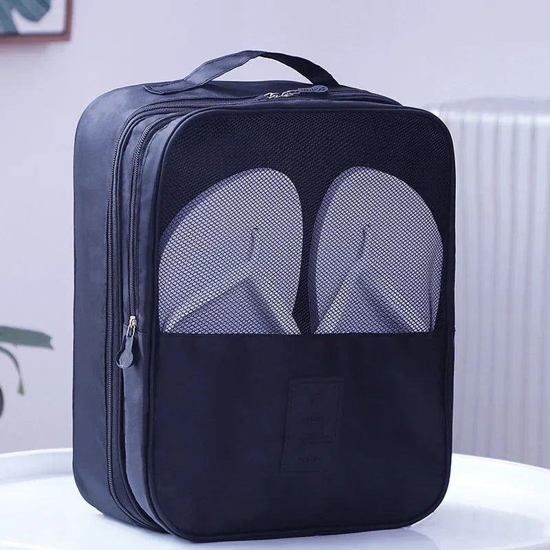 Black travel shoe bag with mesh sections for shoes on a white surface.