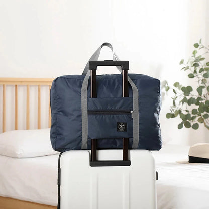 Navy blue folding travel bag with gray handle on a white suitcase in a bedroom setting.