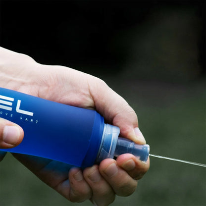 Hand holding a blue water bottle with silicone spout, labeled 'ELS', against a dark background.