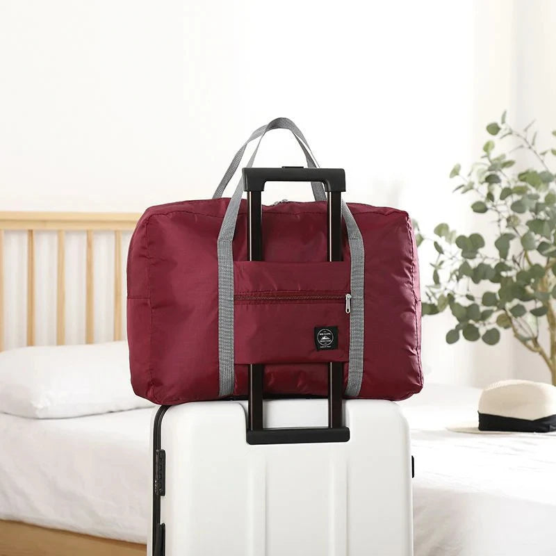 Red folding travel bag with wheels on a white suitcase in a room setting.