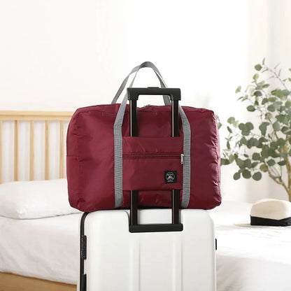 Red folding travel bag with wheels on a white suitcase in a room setting.