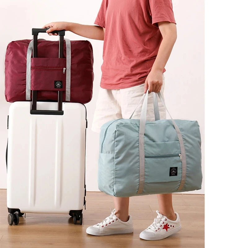 Person holding a red and a light blue foldable travel bag next to a white suitcase.