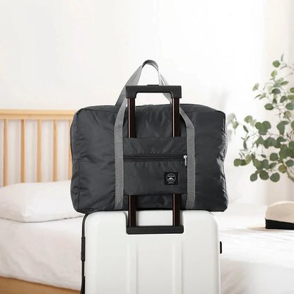 Black folding travel bag with handle on a white suitcase in a bedroom setting