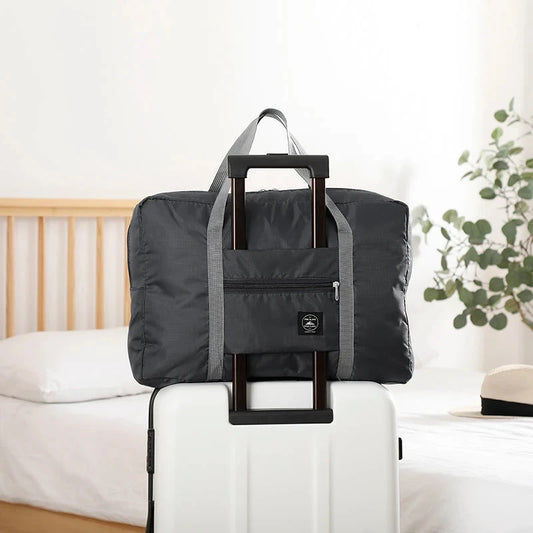Black folding travel bag with handle on a white suitcase in a bedroom setting